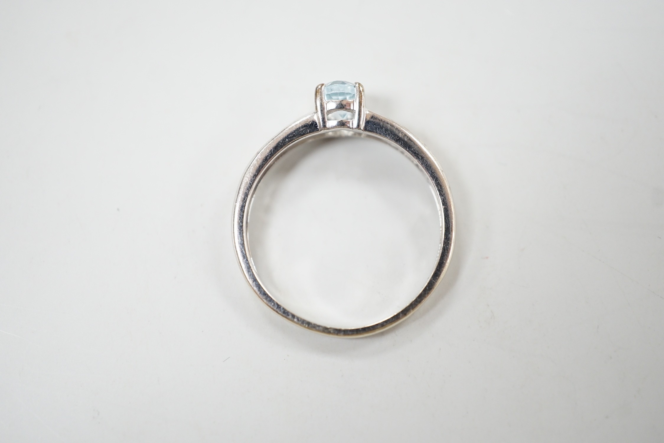 A modern 9ct white gold and oval cut blue topaz ring, with diamond chip set shoulders, size N, gross weight 2 grams.